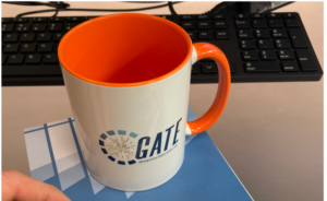 Coffe mug with OpenGate collaboration Logo seen on a computer desk.