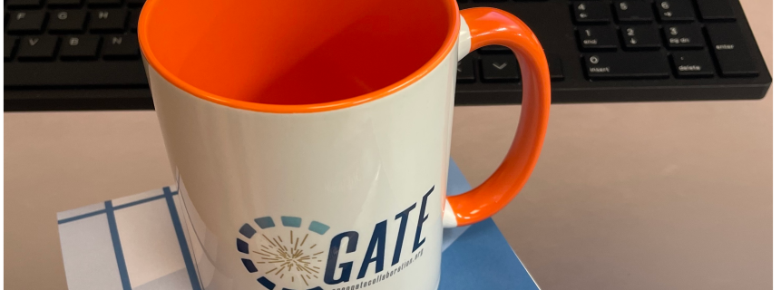 Coffe mug with OpenGate collaboration Logo seen on a computer desk.
